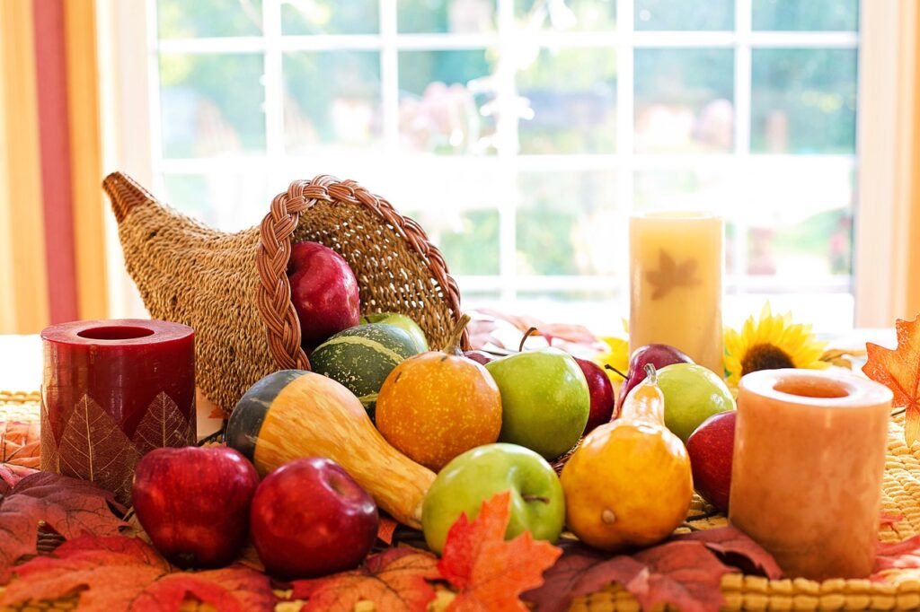 A cornucopia spilling apples and squashes onto an autumnal table with harvest themed candles