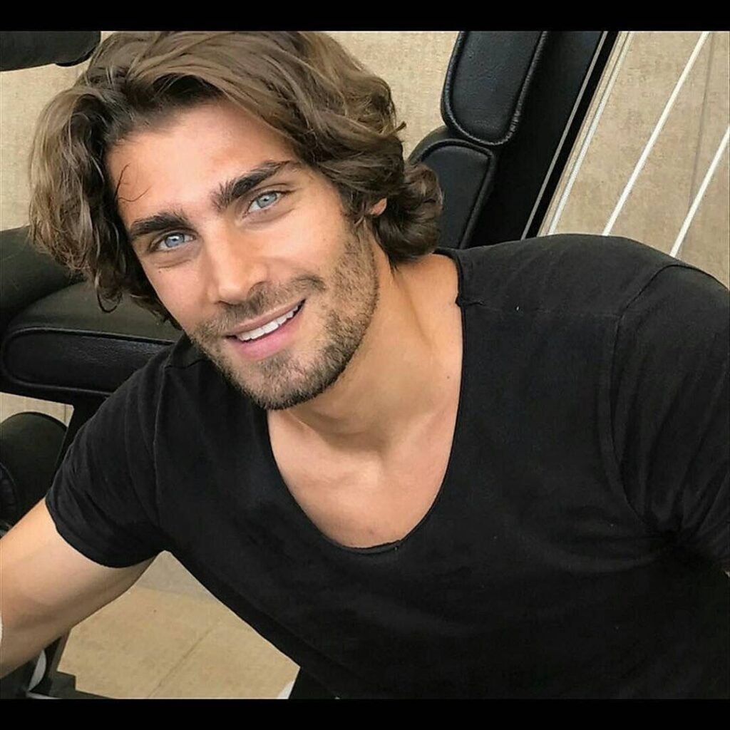 Some stock photo of a Greek guy with a strong chin and wavy hair wearing a black t shirt