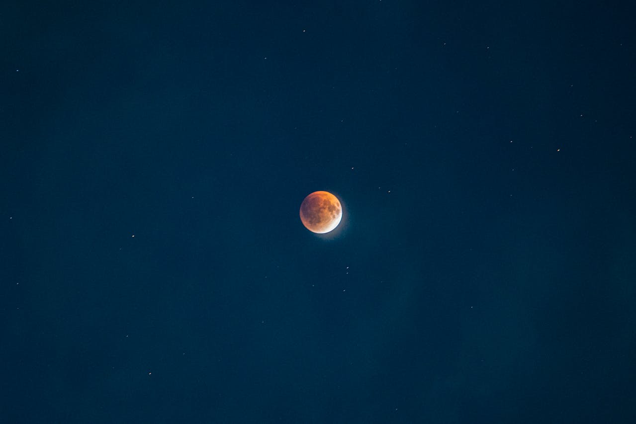 A moon, red with a sliver of white, in a starry dark blue sky