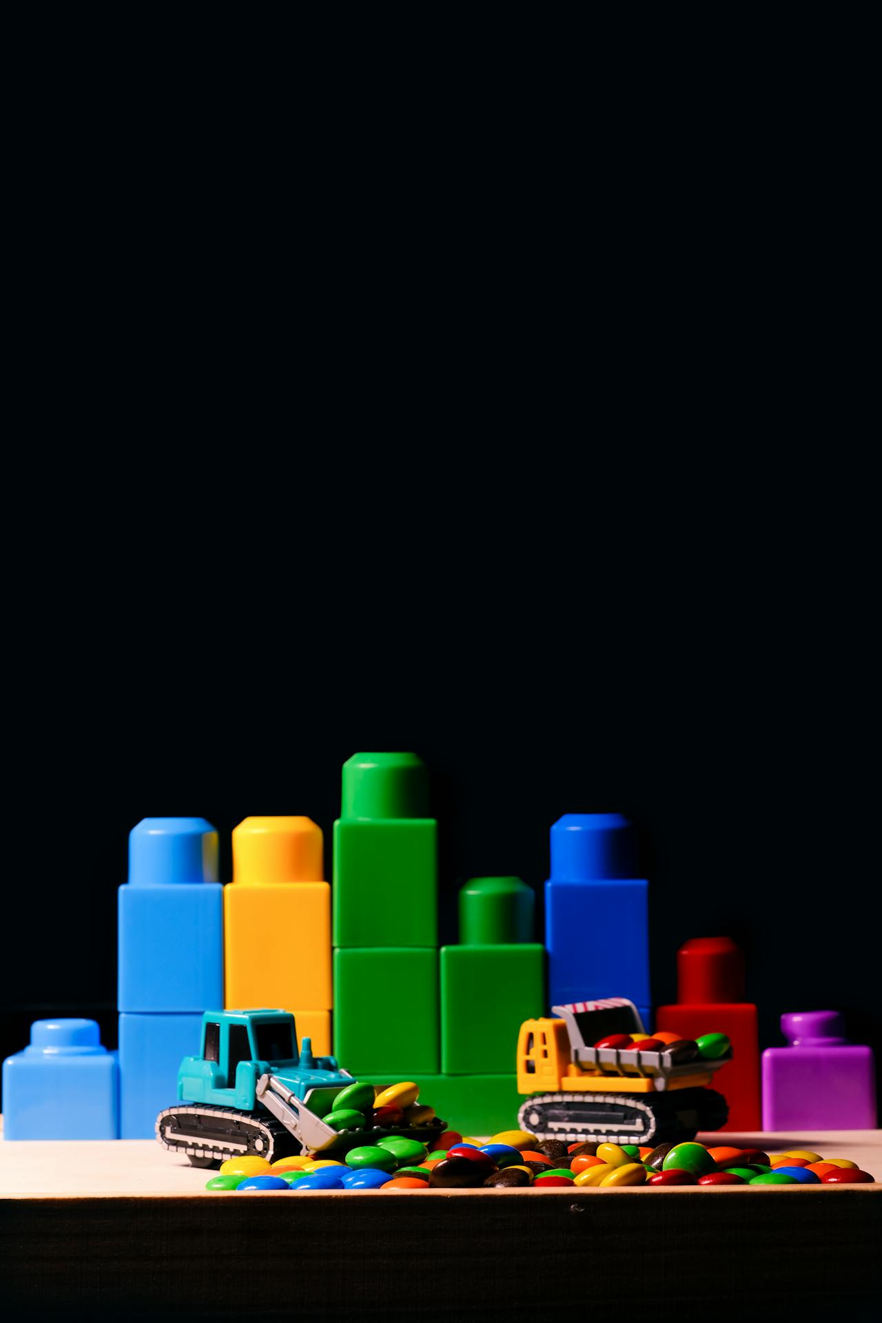 Building blocks and toy bulldozers scooping candy against a black background